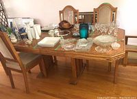 Photo shows oak dining table with pedestal legs and two extension leaves. Various glassware and decorative items are on the table but not included in the lot.