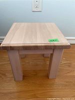 Front view of small wooden side table showing square top and 4 thick legs on hardwood floor