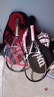 Overview of the two Wilson tennis rackets with their cases and the Roots backpack beside them on the floor, showing the items included in the lot.
