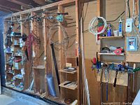 Photo showing various tools stored on wooden shelves and pegboards including cords, wires, small boxes of parts, and other miscellaneous hardware items in basement.