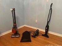 Rocket upright vacuum cleaner with black fabric bag and Dirt Devil handheld vacuum on the floor against a wall