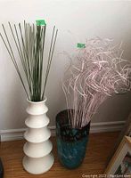 Two decorative vases with artificial reeds and curly sticks, photographed together showing size and detail.