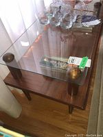 Top angled view showing rectangular glass top supported by four wooden cylindrical posts with rounded caps and wood frame below.