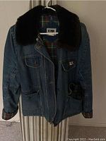 Blue denim women's winter jacket with dark fur collar and plaid lining hung on a hanger.
