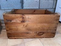 Side view of rectangular wood crate box showing plank construction and natural wood grain with knots and minor wear.
