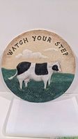 Front view of the round garden stepping stone displaying the cow design and text 'Watch Your Step'.