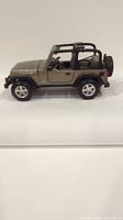 Side profile of Maisto die cast Jeep Wrangler Rubicon in metallic olive green showing open top and detailed wheels.