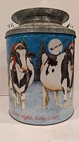 Front view of tin milk can showing cow in Santa hat with snowy pine tree background, 'Silent night, holy cow!' text.