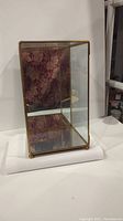 Photo of glass display cabinet showing front and right side with mirrored interior and gold trim.