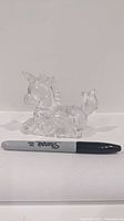 Clear glass or crystal unicorn figurine placed next to a Sharpie marker for size comparison