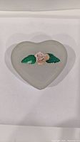 Heart-shaped glass box with a flower and two green leaves on the lid, shown closed.