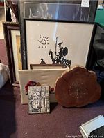 Seven framed art pieces arranged leaning against wall with wood slab clock in front