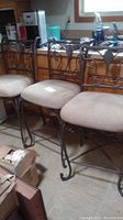 Three metal framed bar stools with beige cushioned seats lined in a kitchen.