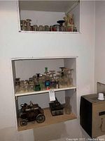 Shelves with an assortment of clear and colored glassware including wine glasses, shot glasses, and whiskey glasses. Lower shelf contains decorative metal carriage and wooden box.