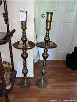 Two tall brass candle holders standing on hardwood floor near a door.