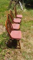 Four wooden chairs with curved spindled backs and pinkish-red cushioned seats arranged outdoors on grass.
