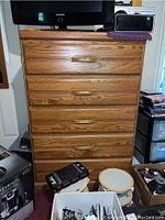 Full front view of the tall chest of drawers with five drawers, wood grain finish, and brass inset handles.