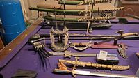 Photo of multiple decorative swords with ornate sheaths, a stand holding swords, and a knuckle-duster style weapon with prongs