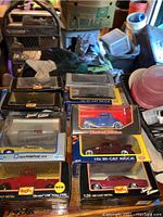 Photo showing seven die-cast replica model cars in their original boxes including Chevrolet, Pontiac, and Ford models arranged on a surface.