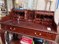 Full front view of mahogany roll-top desk showcasing cubby hole organizers and two large drawers with brass handles under the desktop.