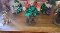 Top view showing several clown figurines dressed in colorful satin-like fabrics with painted faces and a small dark decorative piece in front.