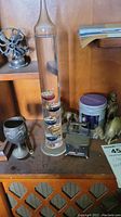 Photo showing Galileo thermometer, small metal figurines, and container on wood shelf