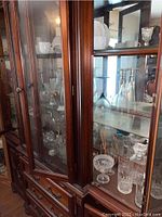 Glassware including wine glasses, decanters, clear glass bowls, displayed in a wooden cabinet with glass doors