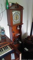 Full view of the grandmother clock showing the wooden case and decorative clock face.