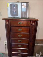 Front view of wooden jewelry cabinet with six drawers and massage pillow box on top.