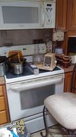 Kitchen counter with microwave above stove, various cookware including pot, pans, coffee mugs, and a small food processor on stovetop