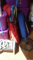 Photo showing various outdoor sports and camping items including tent/badminton bag, blue cylindrical item, tripod and umbrella stand.