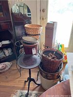 Overview of multiple metal plant stands, woven and plastic pots, with bathroom scale and other items visible