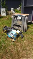Metal sawhorse, black toolbox, portable vacuum box, tool organizer, and car cleaning kit arranged on grass outside.
