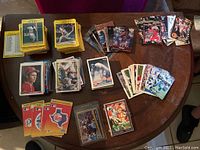 First photo showing multiple stacks of sports cards on a wooden table with different sports represented including baseball, basketball, football, and NASCAR.