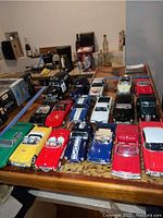 Top and side view of 18 toy replica cars in various colors on a table with other household items in background.
