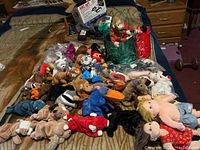 Wide assortment of Beanie Babies and plush toys on bed with bags and miscellaneous items