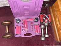 Wide image showing purple exercise kit, copper-colored dumbbells, silver dumbbells, and red stretch rope