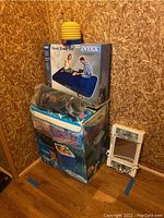 Stacked boxed items: Intex air mattress box on top, thermoelectric cooler box below, with Windmere light-up mirror standing against the wall.