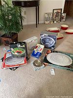 Overview of several serving items on carpet including boxed salad bowl, platters, basket, and utensil set