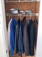 Closet rack with five men's coats hanging, various colors and materials, and two New England Patriots hats placed on top shelf
