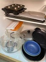 Photo of muffin pans, baking trays, glass measuring cups, bowls, ice cube trays, and a wire cooking rack on a shelf.