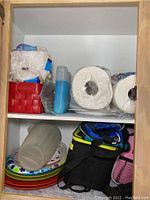 Shelf with two large rolls of paper towels, red lunchbox, plate stacks, and insulated lunch bags