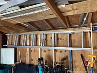 Full view of the aluminum extension ladder stored horizontally in the shed against wooden wall and ceiling structure.