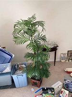 Full view of faux palm tree showing detailed green fronds and wooden planter box on carpeted floor.