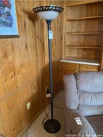 Full view of black metal floor lamp with base, pole, and decorative openwork metal ring top, standing next to a couch and wood paneling.