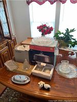 Wide shot of dining table showing all items in the lot including cut glassware, boxed ice bucket, chrome butter dish, frosted glass bell, and assorted cutlery.
