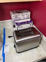 Photo of stainless steel Bella two-slot toaster on kitchen counter with original boxed George Foreman Hot Metal griddle and Rival hand mixer behind it.