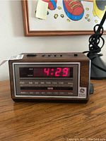 Front view of vintage GE clock radio showing digital time display at 4:29 and AM/FM frequency scale, placed on wooden surface near a black desk lamp base.