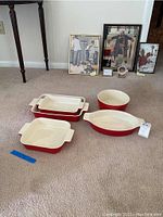 All five baking dishes arranged on the carpet showing their colors and shapes with framed art in the background.