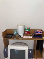 Wooden shelf with white cylindrical desk lamp, playing cards, black calculator, metal stapler, classic silver service bell, and wood shelf. Computer monitor visible below shelf.